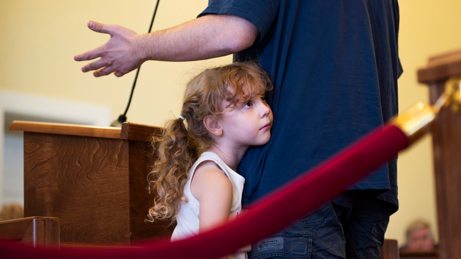Janey Eagle rests against her dad, Marc, while he is giving a speech to the board members during a quarterly meeting for the Randolph County Library of Trustees at the historic courthouse in downtown Asheboro, NC on Thursday, Oct. 9, 2025. The meeting presented a large crowd of community members who debated the placement of the children's book on transgender awareness titled "Call Me Max" by Kyle Lukoff in the public library. The board members decided to keep the book in the library following the end of the meeting. (Photo by Sollyn Lindsay).